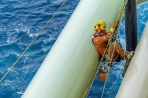 Abseiler wearing complete Personal Protective Equipment hanging and holding his life lines using full body harness for painting activities at pipeline.