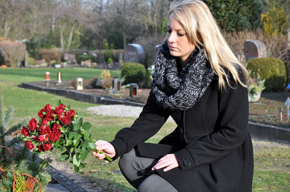Sad woman woman laying flowers on a grave.